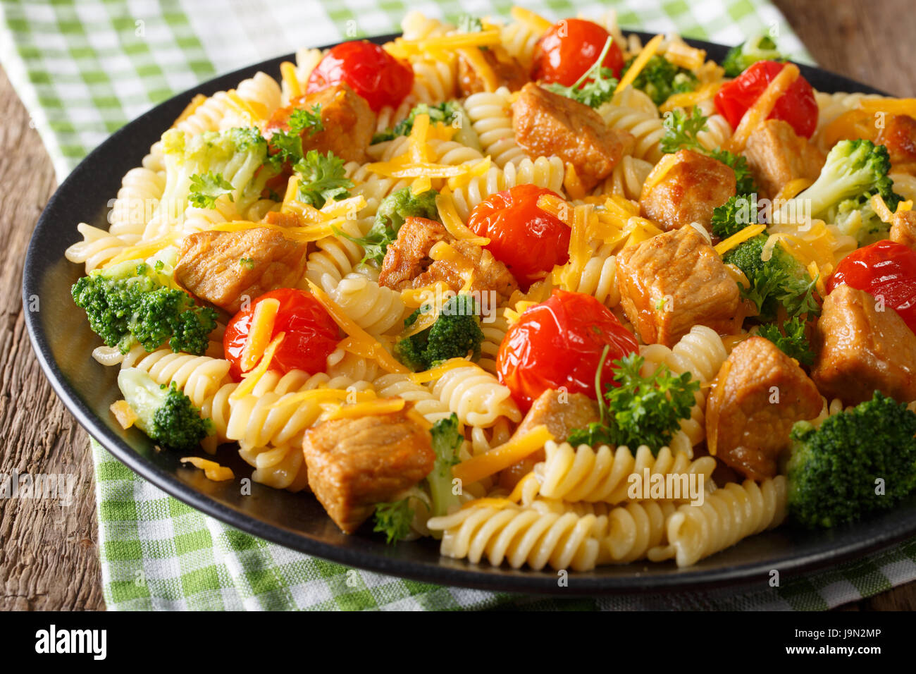 Leckeres Essen: italienische Pasta mit Scheiben von Schweinefleisch, Brokkoli, Tomaten und Cheddar Nahaufnahme auf einer Platte. horizontale Stockfoto