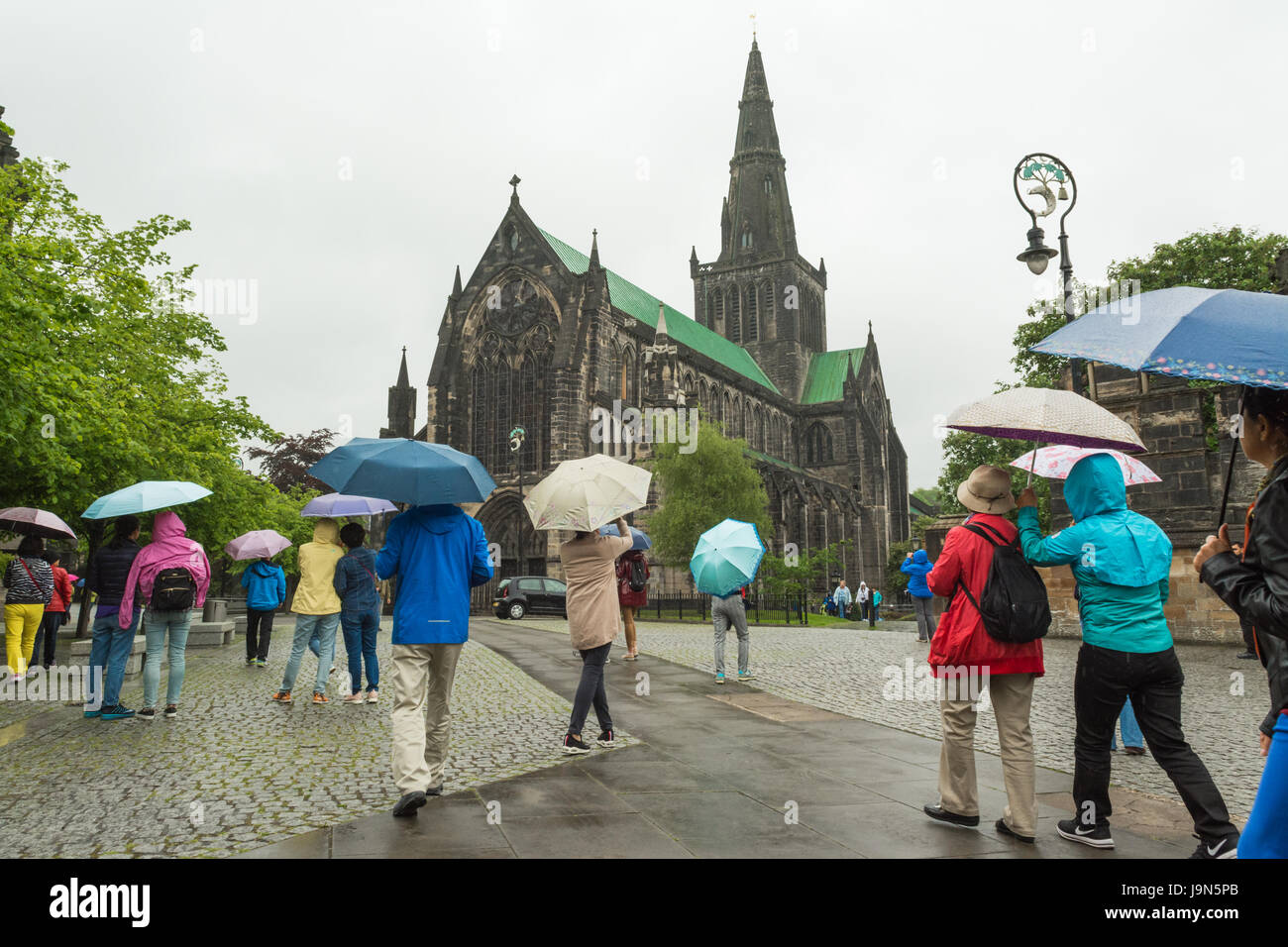 Glasgow Regen - asiatische Touristen mit bunten Sonnenschirmen außerhalb der Kathedrale von Glasgow, Schottland, Großbritannien Stockfoto