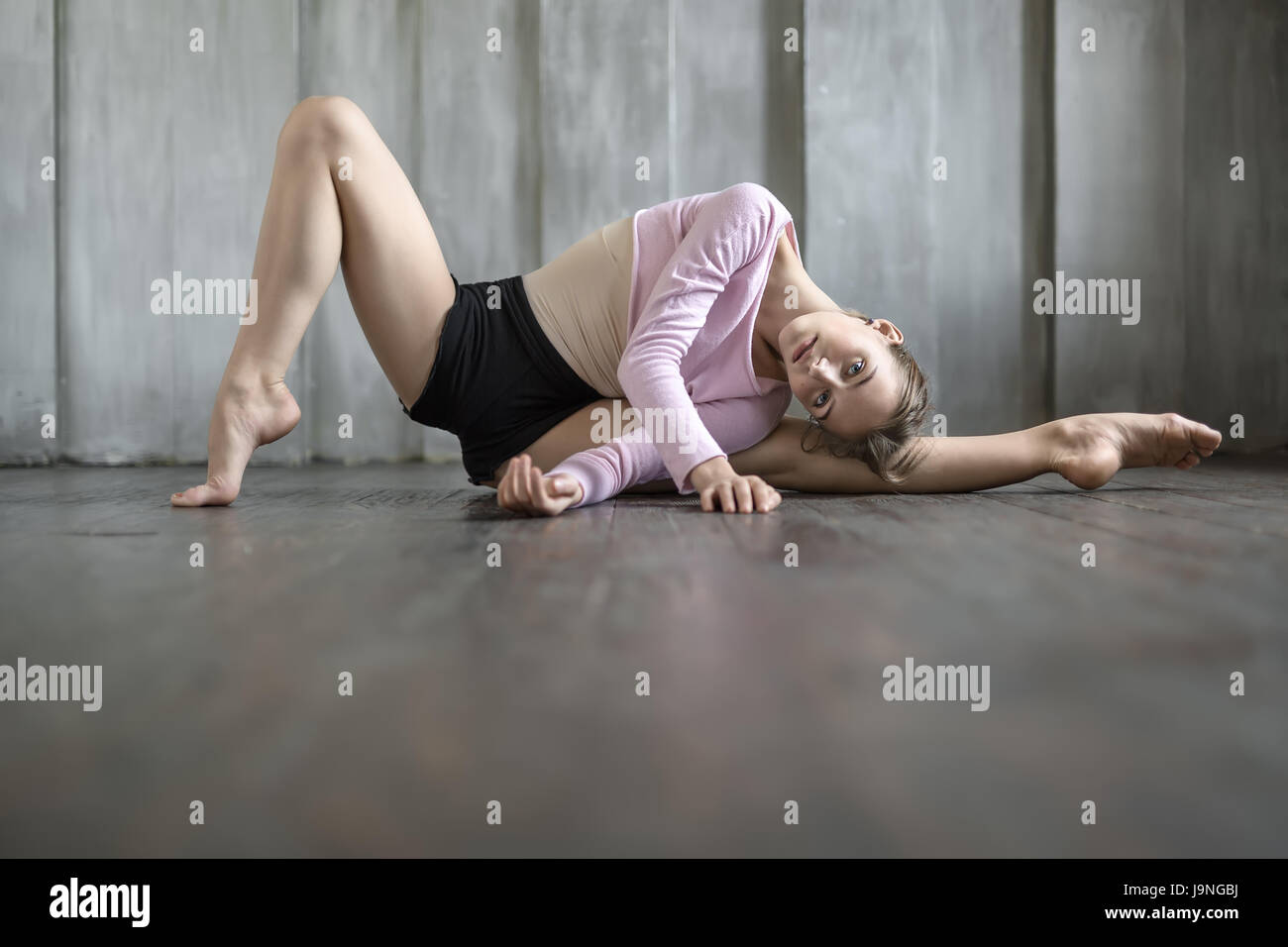 Schöne Ballerina Tanz Verschleiß liegt auf dem linken Bein gestreckt auf einer Etage auf die strukturierte Wand Hintergrund. Ihr rechtes Bein ist im Zehenbereich, Arme gekreuzt. Stockfoto