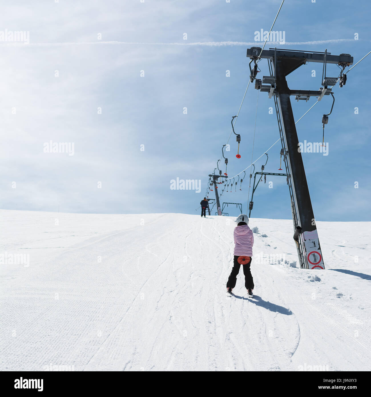 Anfänger Mädchen mit Skiern steigt mit Skilift Stockfoto