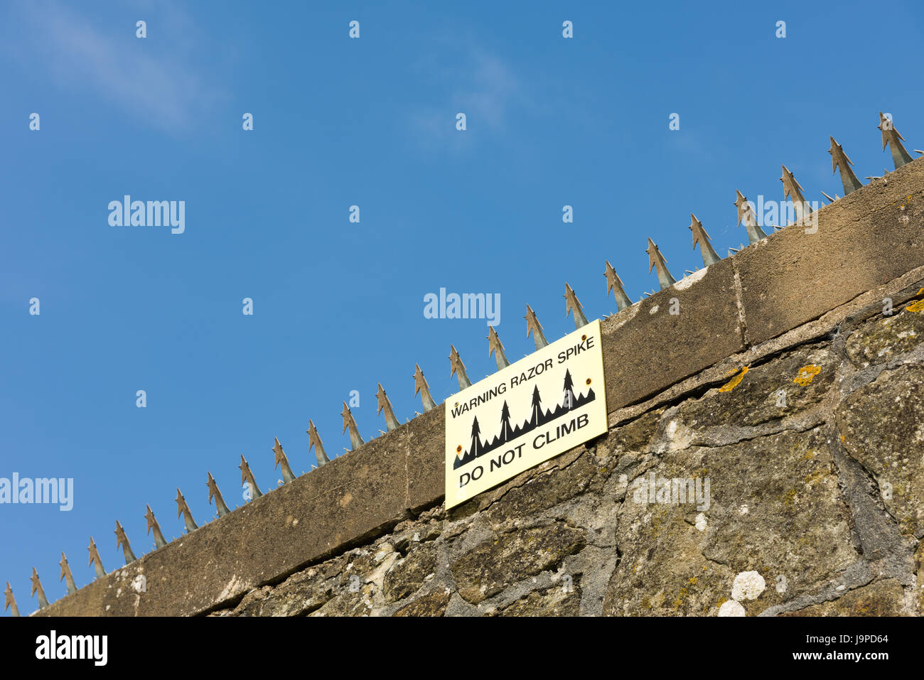 Rasiermesser Stacheln auf der Oberseite eine Steinmauer mit einer Zeichen-Warnung steigen nicht. Stockfoto