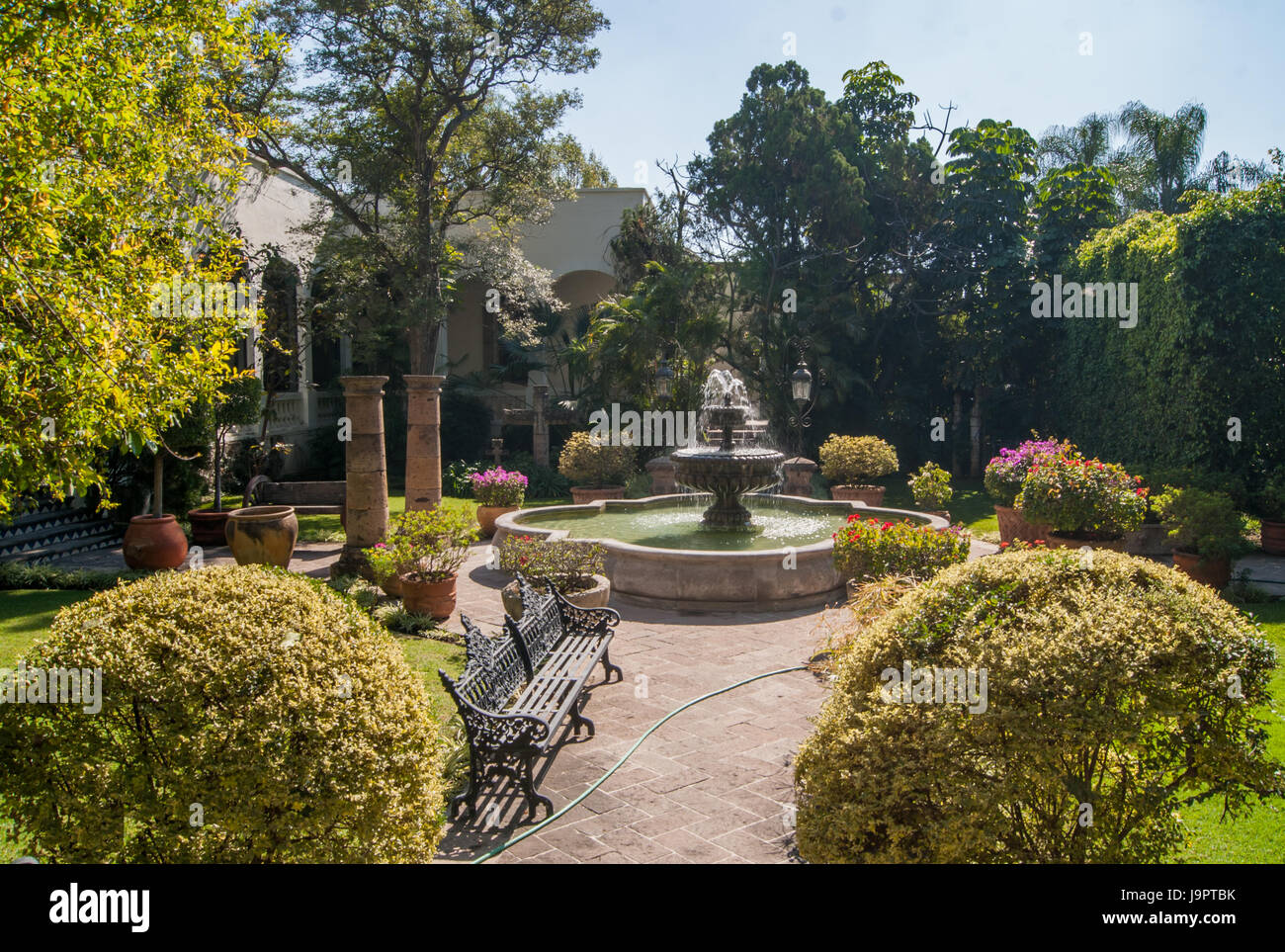 Eine schöne Gartenanlage mit einem großen Brunnen, Bänke und Zierbäume und Sträucher. Stockfoto