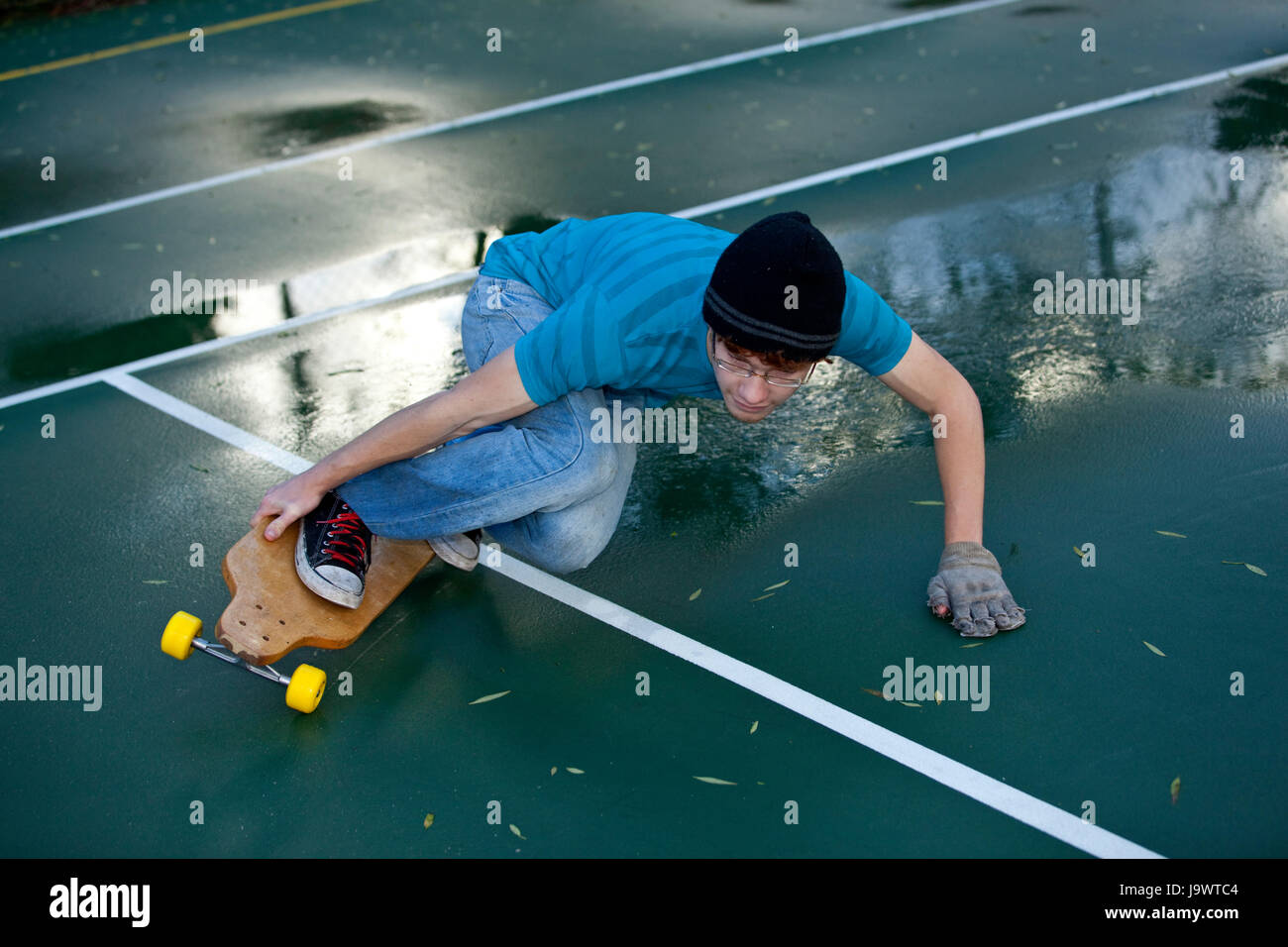 Teenager mit seinem Longboard im Tennis Hof Skaten Stockfoto