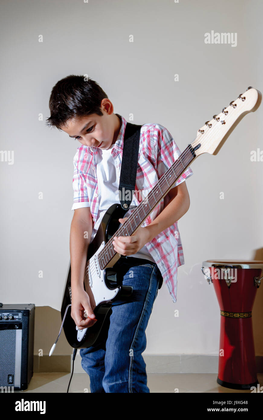 Teen Boy, der zu Hause elektrische Gitarre spielt, isoliert vor einem weiß-grauen Hintergrund, fängt die Leidenschaft und Energie der Jugend in der Musik ein Stockfoto