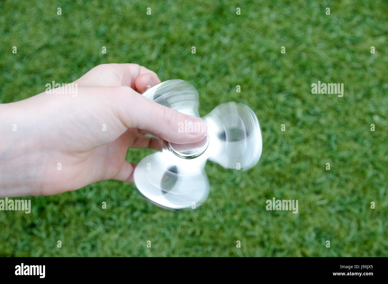 Eine Childs Hand Spinnen Silber zappeln Spinner vor einem grünen Hintergrund Stockfoto