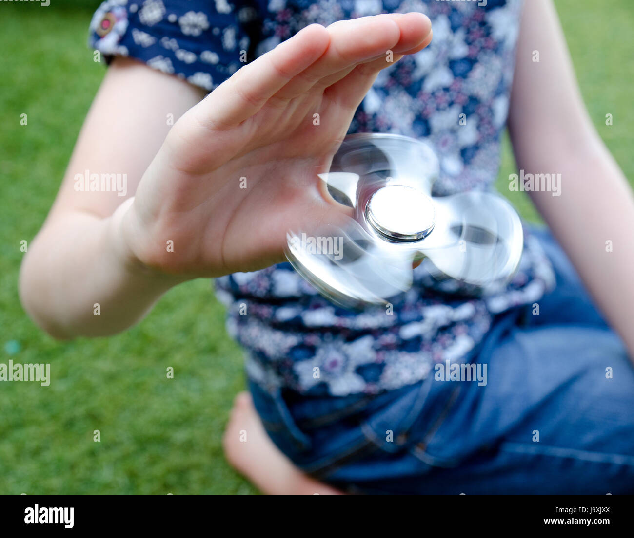 Ein Kind spielt mit einem drehenden Fidget Spinner im Garten Stockfoto