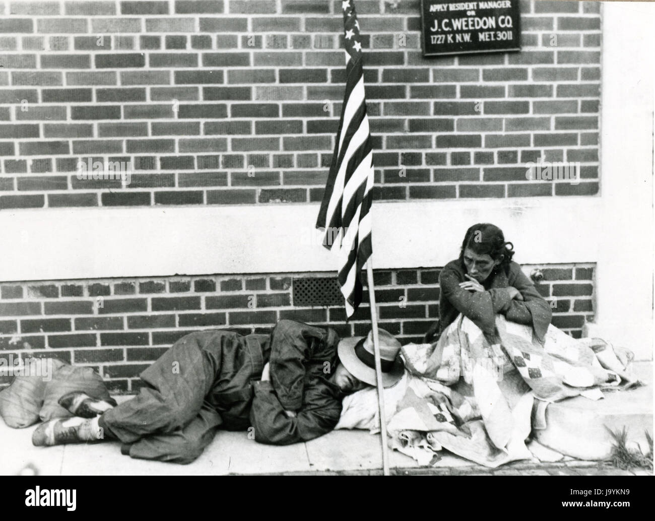 Washington, D.C., Juli 1932 - Veteran des ersten Weltkriegs und seiner Frau ruhen auf einem Bürgersteig unter ihrer Flagge und decken, wo sie schlief nach einer Zwangsräumung durch Truppen aus ihren Vorstadt mit anderen Bonus-Demonstranten. Stockfoto