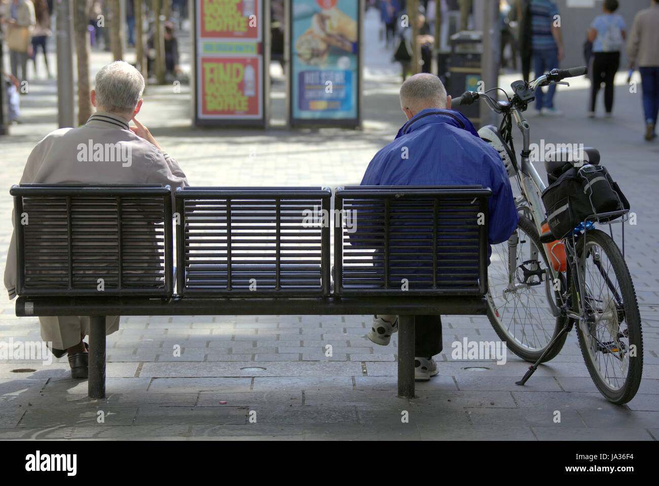 auf einer Bank sitzend von hinten zwei Männer mittleren Alters und ein Fahrrad angesehen Stockfoto