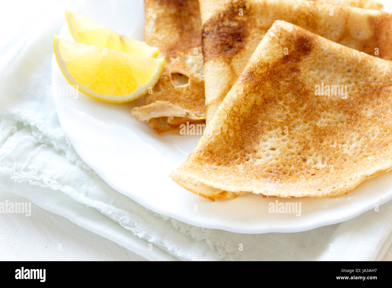 Crepes Suzette mit Zitrone auf weißen Teller über weißem Hintergrund ...