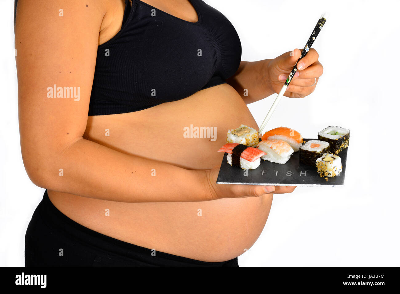 Eine schwangere hält einen Teller mit leckeren Sushi mit ihren Stäbchen in den Startlöchern. Stockfoto