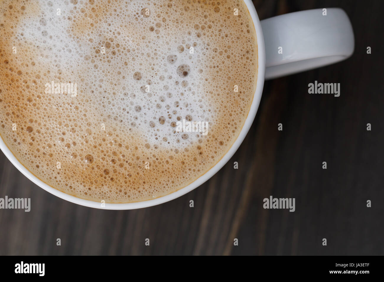 Draufsicht auf eine weiße Tasse Cappuccino auf einem schwarzen Holztisch. Nahaufnahme, Makro erschossen. Kopieren Sie Raum. Stockfoto