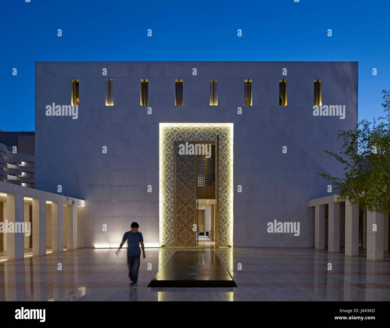 Twilight-Ansicht mit einsame Figur und Eingang. Jumaa Moschee, Doha, Vereinigte Arabische Emirate. Architekt: John McAslan & Partner, 2017. Stockfoto
