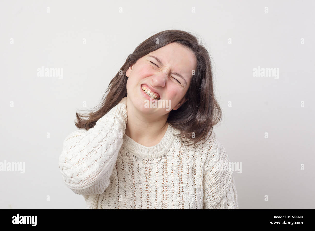 Mädchen in einem weißen Pullover und lange Haare zerknittert Gesicht, Nacken-Schmerzen leiden Stockfoto