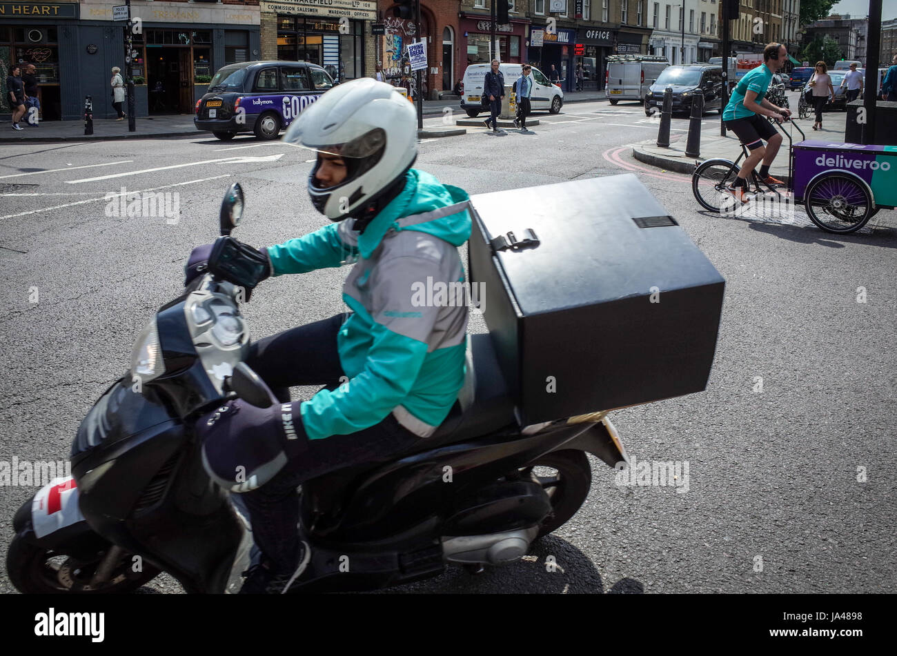 Zwei Deliveroo Essen Lieferung Kuriere passieren im Zentrum von London, eine auf einem Roller, der andere ein Lastenfahrrad Stockfoto