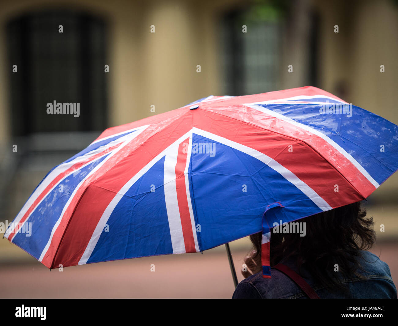 Eine touristische trägt einen Union Jack Regenschirm während einer Regendusche im Zentrum von London, Großbritannien Stockfoto