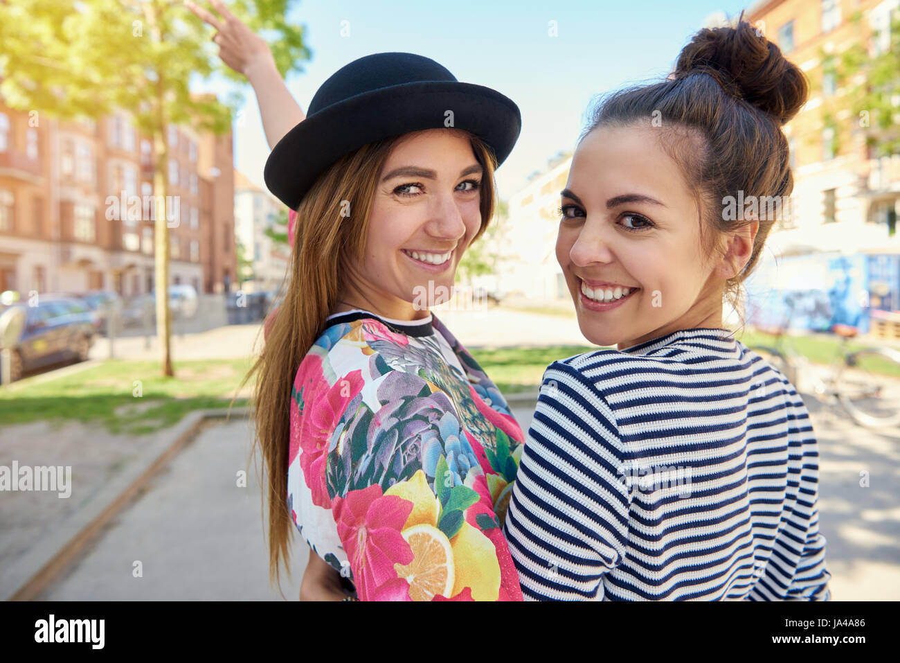 Zwei hübsche Frauen mit schönen, niedlichen Lächeln zurück über die Schulter in die Kamera zu schauen, Nahaufnahme Oberkörper Aussicht in der Stadt Stockfoto