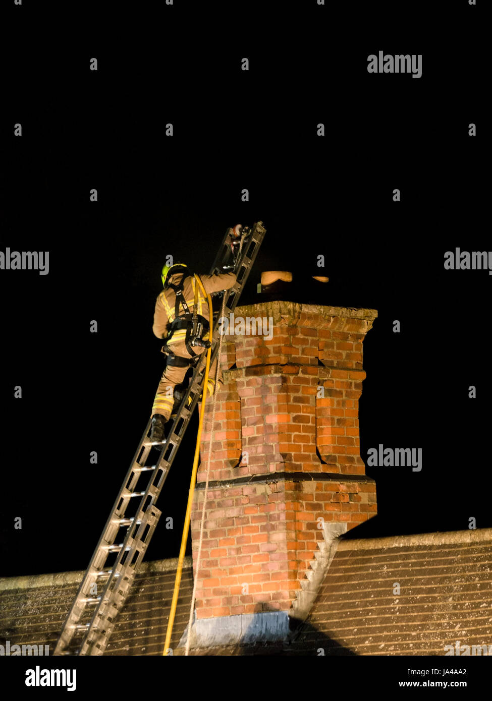 Flutlicht Feuerwehrmann auf Leiter nach nächtlichen Hausbrand Schornstein Stockfoto