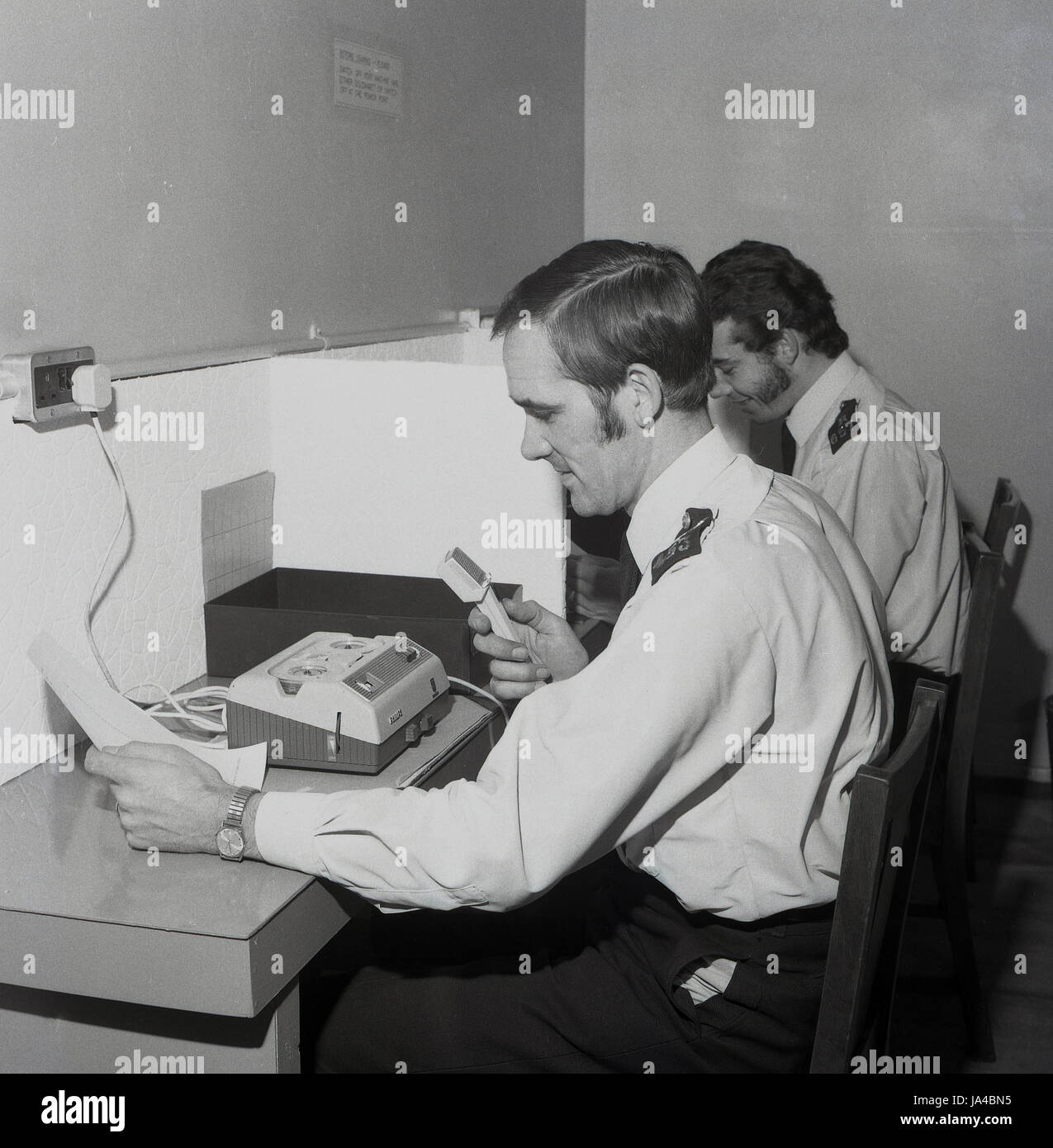 In den 1970er Jahren saßen zwei uniformierte Polizeibeamte an Ständen, die die neuen Diktafon- oder Tonaufzeichnungsmaschinen benutzten, die der Metropolitan Police Service in dieser Ära einführte, um die Aussagen eines Verdächtigen oder Kriminalberichte zu erstatten. Stockfoto