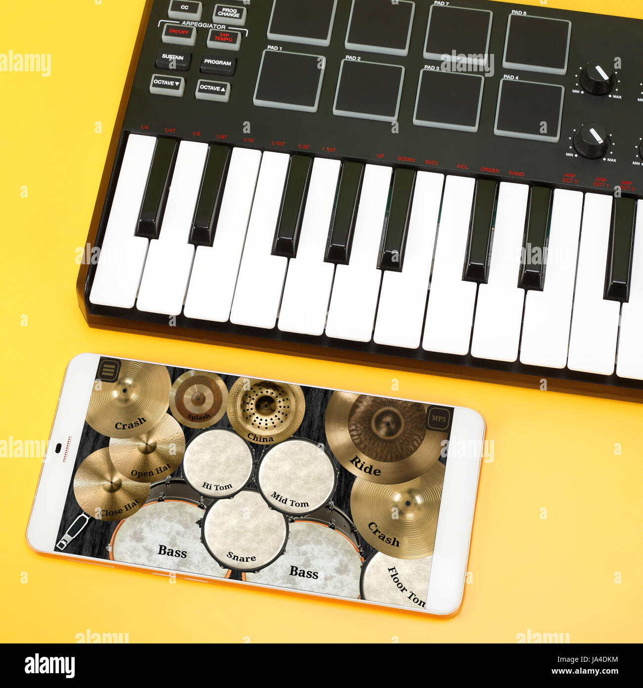 Musikinstrument - MIDI-Keyboard und Schlagzeug auf dem Bildschirm des Smartphones für die Komposition der Musik. Auf einem gelben Hintergrund. Stockfoto