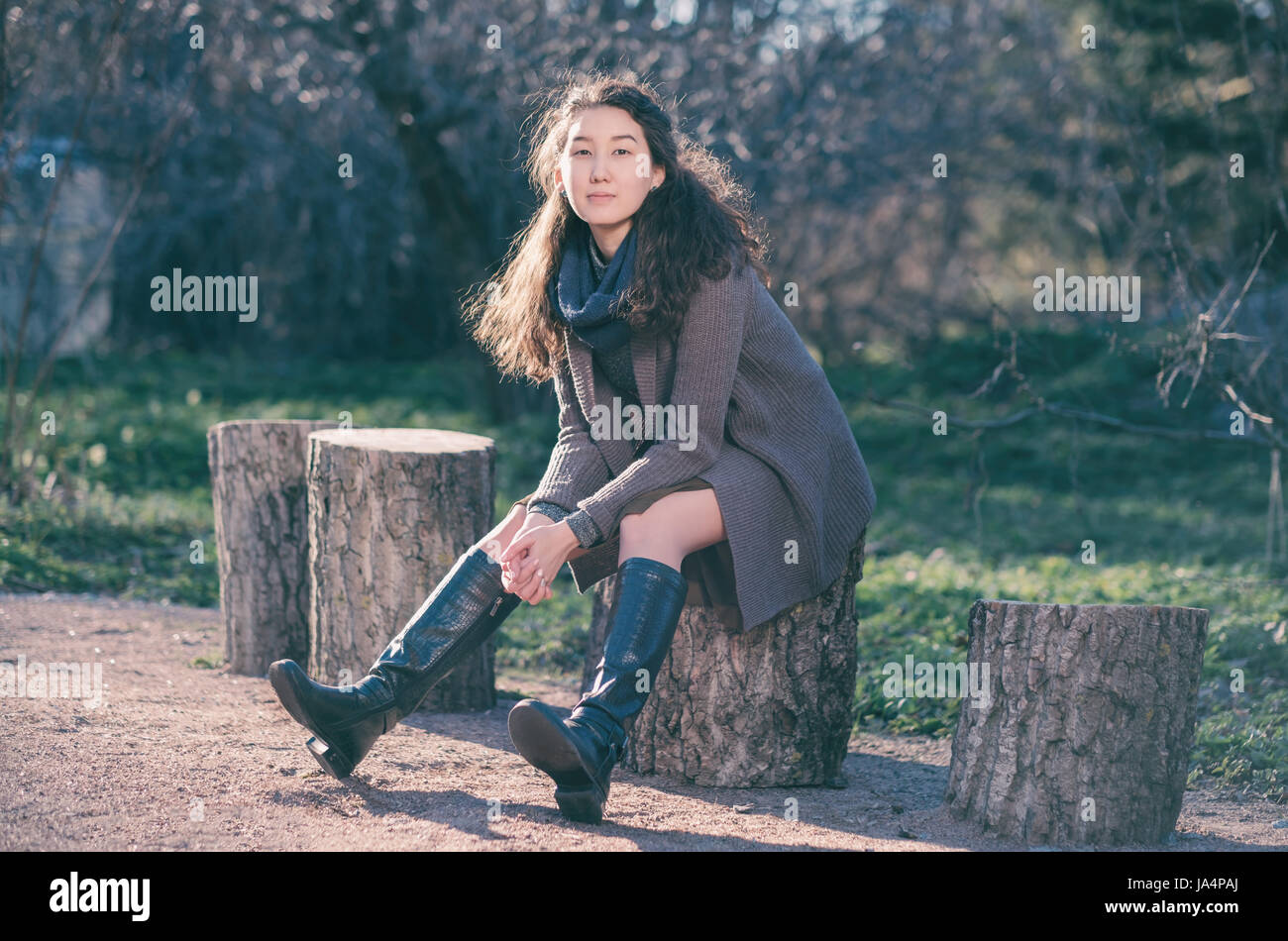 Eine schöne Asiatin liegt in einem Park auf einem Baumstumpf und entspannt ihre Beine nach vorne. Genießen Sie die Ruhe am Stadtleben. Stockfoto