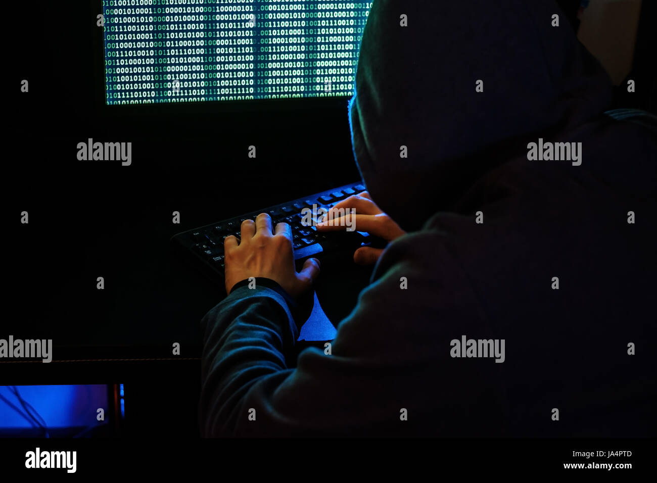 Der Mann in der Haube prüft den Schadcode auf der Tastatur. Cyberkriminalität über das Internet. Stockfoto