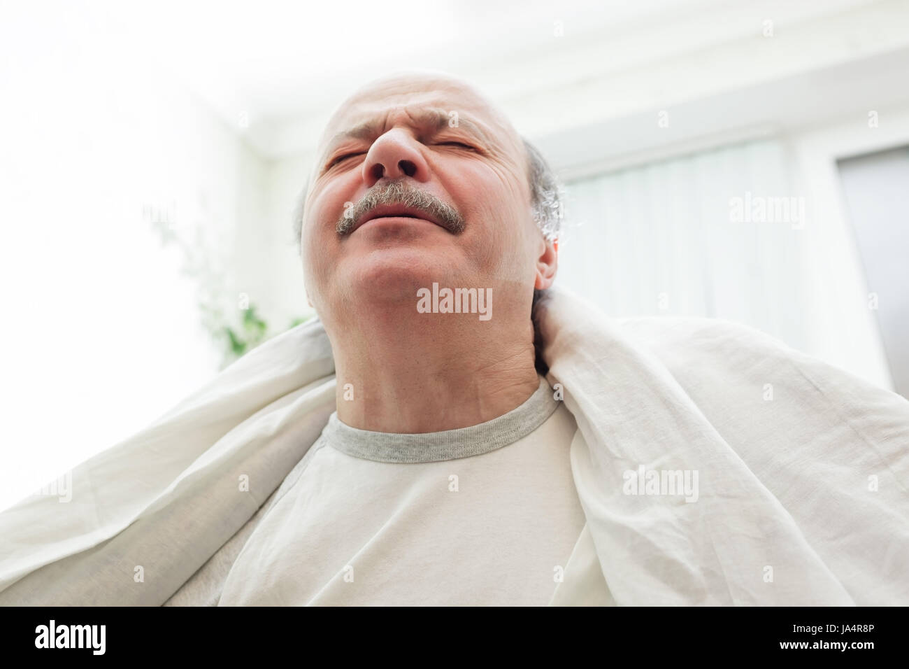 Ein älterer Mann leidet unter Schmerzen und Stress. Er warf eine weiße Decke über die Schultern. Stockfoto