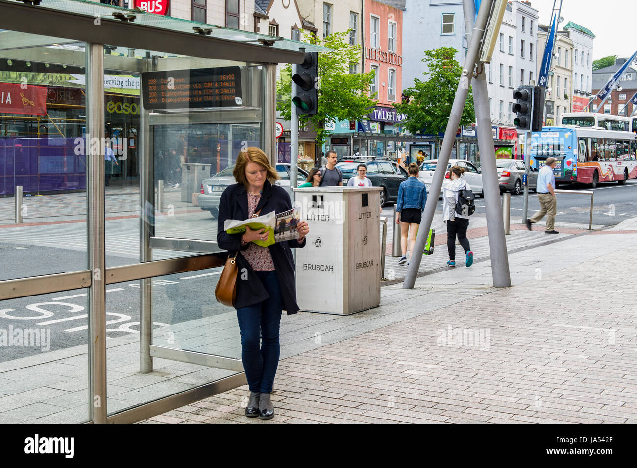 Frau liest das Magazin an einer Bushaltestelle in Cork, Irland. Stockfoto