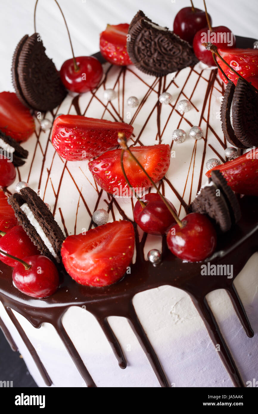 Mousse-Torte mit frischen Erdbeeren und Kirschen, dekoriert mit Keksen und Schokolade Nahaufnahme. vertikale Stockfoto