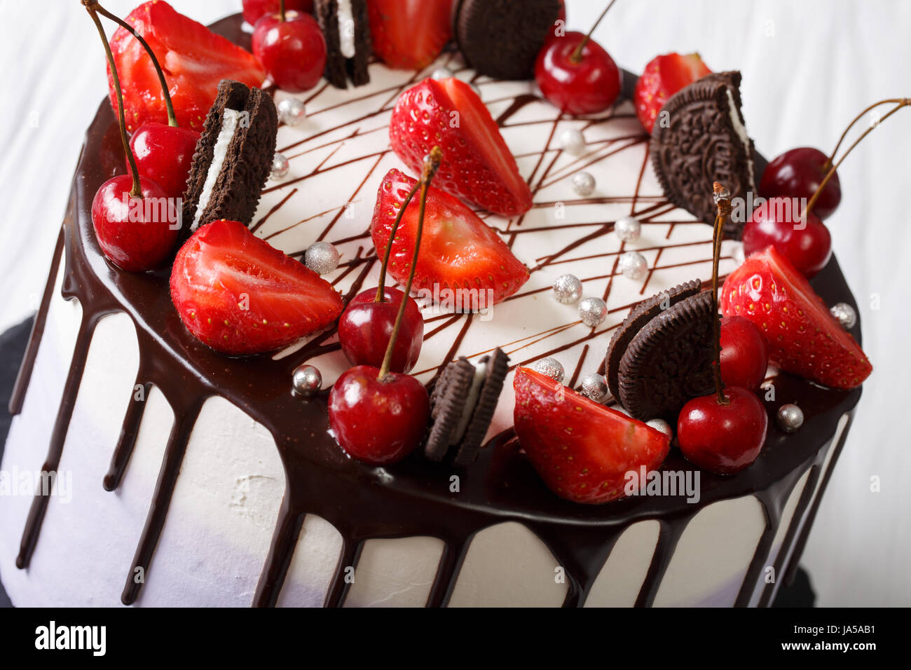Mousse-Torte mit frischen Erdbeeren und Kirschen, dekoriert mit Keksen und Schokolade Nahaufnahme. Horizontale Stockfoto