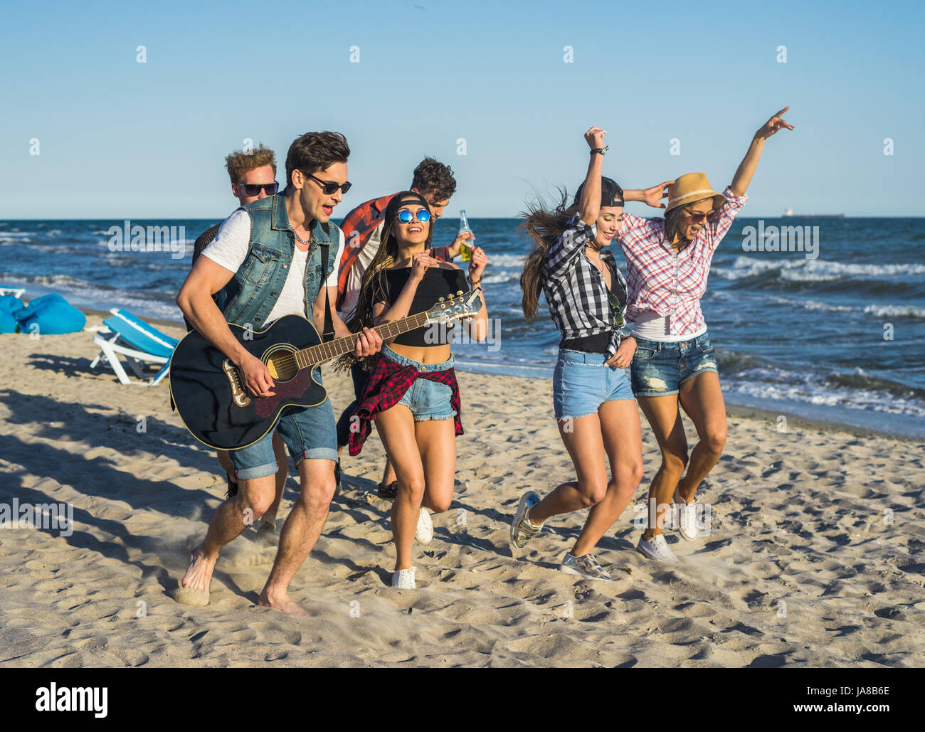 Party am Strand mit Gitarre. Freunde, die zusammen tanzen am Strand Stockfoto