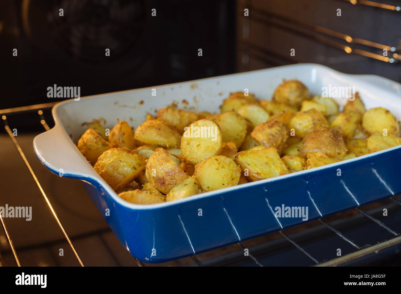 Backkartoffeln mit Kurkuma und anderen Gewürzen in der Pfanne rösten. Ofen auf Hintergrund Stockfoto