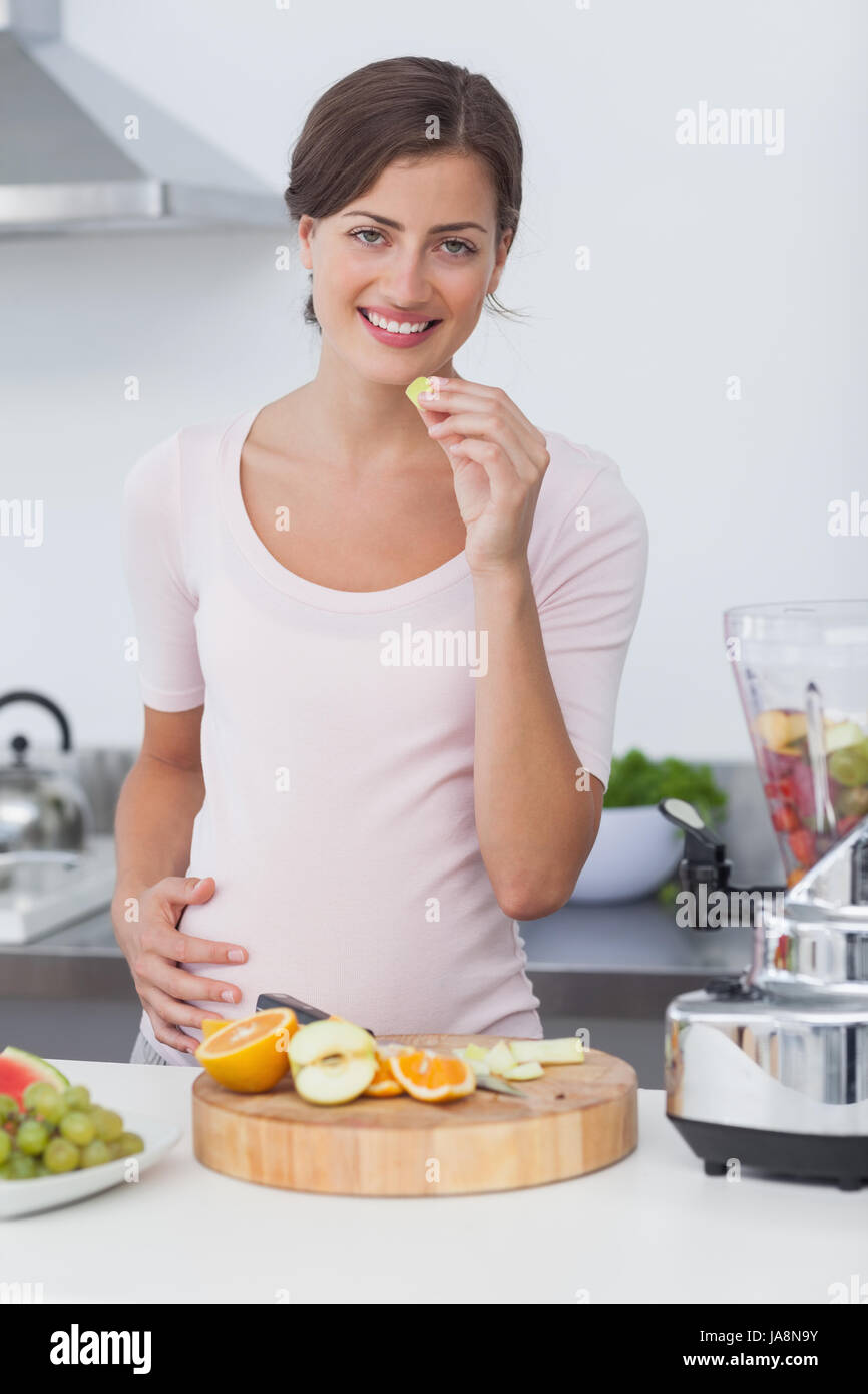 Schwangere Frau eine Traube Essen, während der Vorbereitung ein Fruchtcocktail Stockfoto