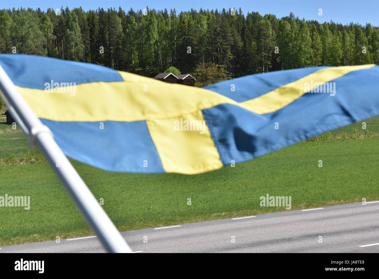 Schwedische Landschaft mit roten Holzhäusern und der schwedischen Flagge, die an einem hellen, sonnigen Sommertag im Vordergrund winkt Stockfoto