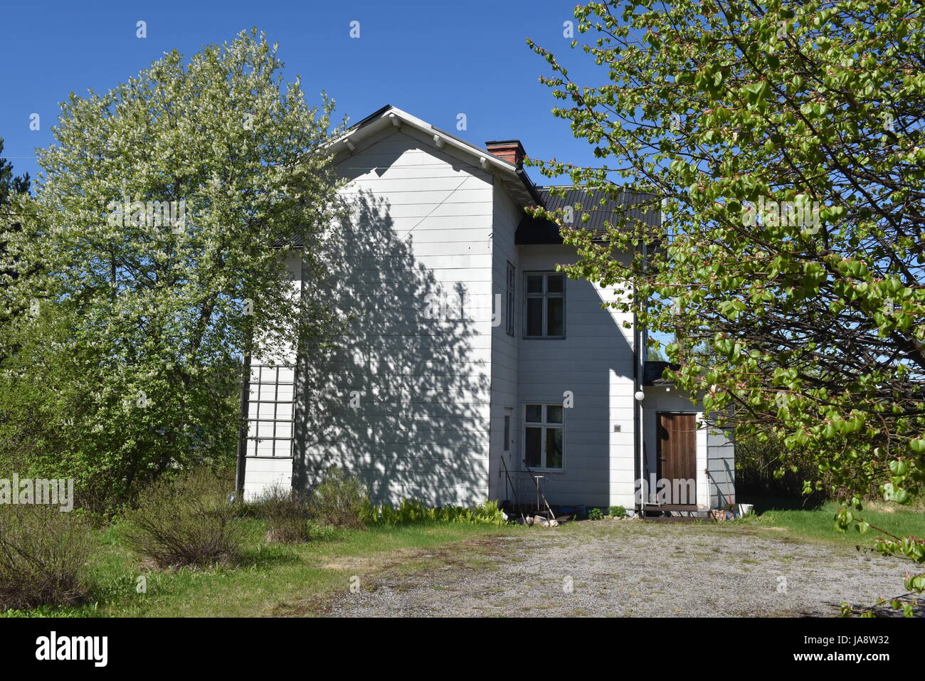 Traditionelles weißes Holzhaus im ländlichen Schweden an einem sonnigen Frühlingstag, umgeben von Bäumen unter einem klaren blauen Himmel Stockfoto