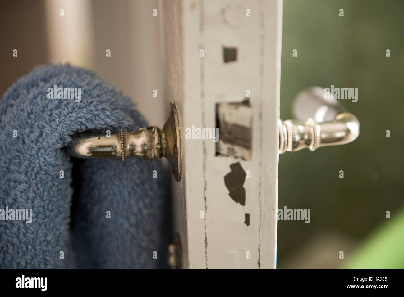 Blaues Handtuch, das an einem alten Metalltürgriff in einem Haus hängt, mit weichem natürlichem Licht aus einem nahe gelegenen Fenster Stockfoto