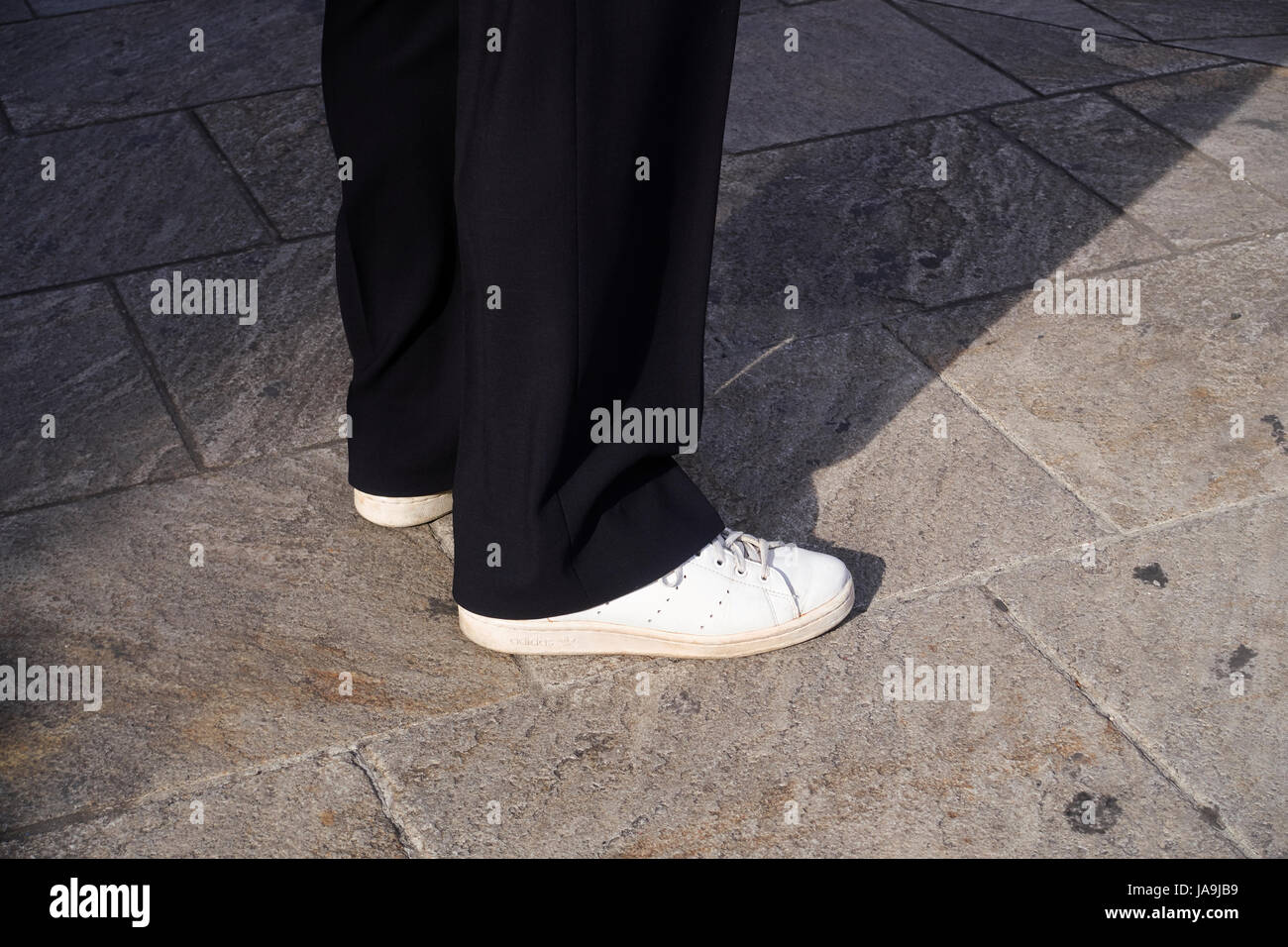 Mann stand auf dem Bürgersteig, Detail der Beine und die Füße. Er trägt ein paar weiße Turnschuhe Stockfoto