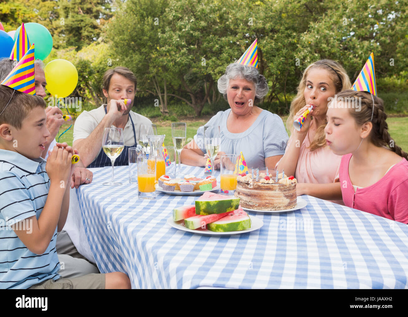 Familie kleine Mädchen Geburtstag außerhalb an Picknick-Tisch weht Partei Hörner Stockfoto