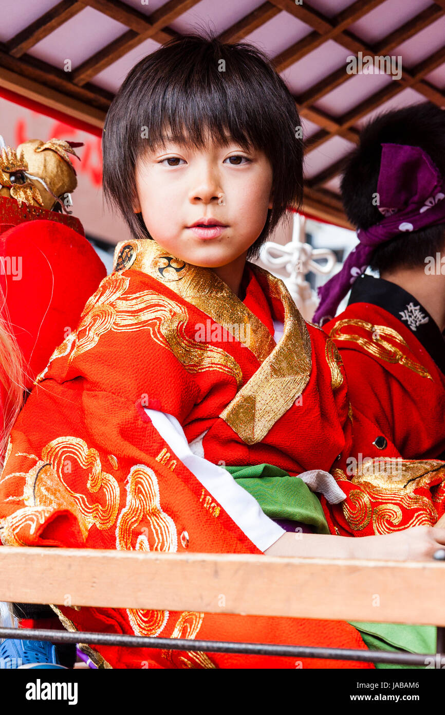 Asiatische, Japanische Junge Kind, 9-10 Jahre, direkt an Viewer mit einem Fragen, Ausdruck. Tragen rote und goldene yukata Jacke. Auge - Kontakt. Stockfoto