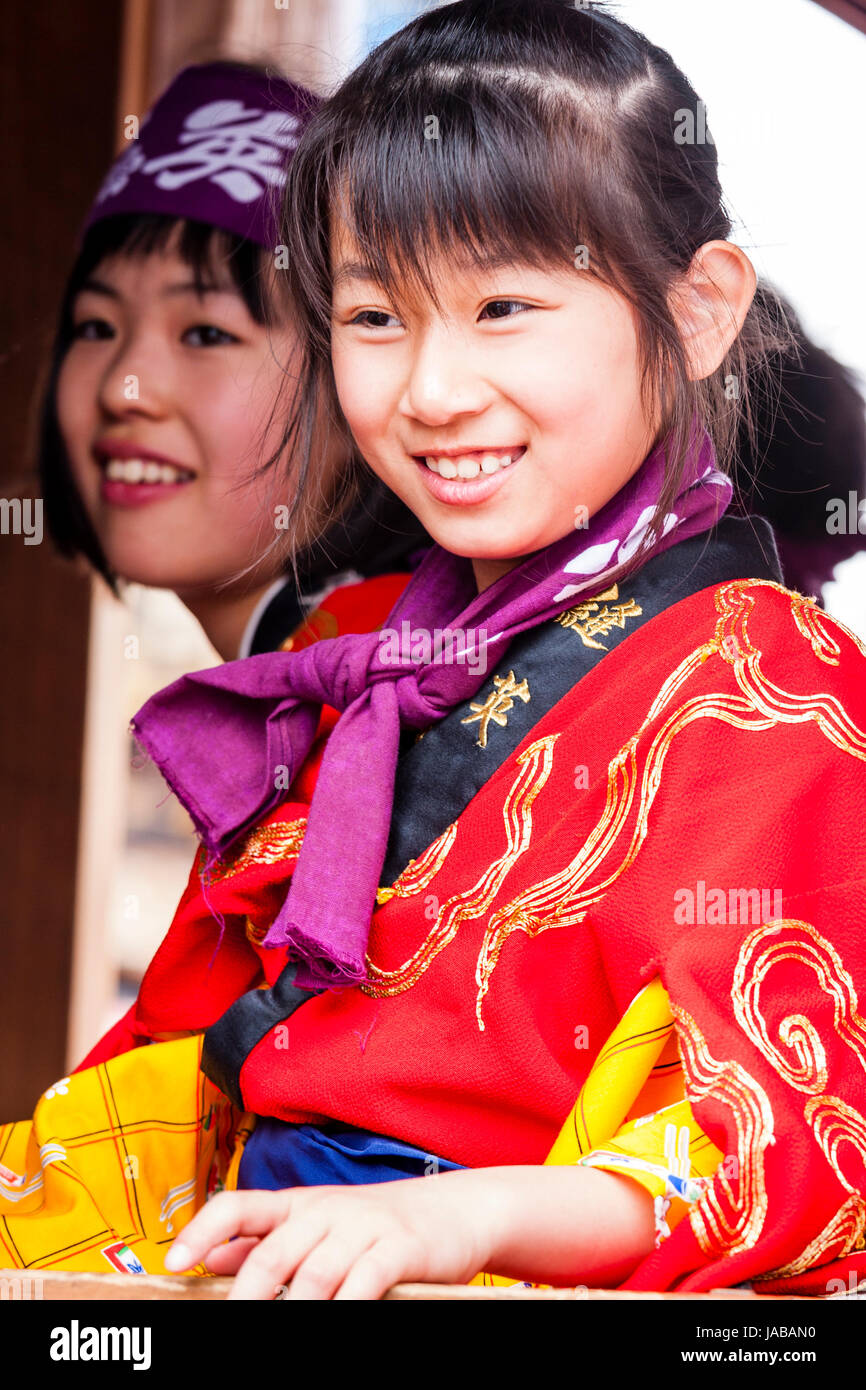 Japanisch, asiatische Kinder, zwei Mädchen, 9-10, nebeneinander sitzen, sowohl in Rot als YUKATA als Teil eines Festivals. Close Up, beide lächelnd, glücklich. Stockfoto