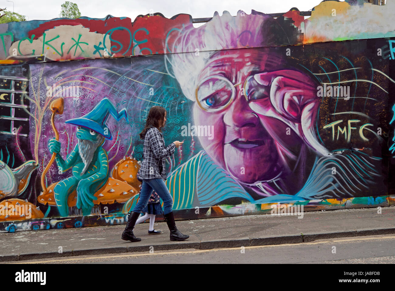 Eine Frau und ein junges Mädchen Fuß durch Graffiti Darstellung einer alten Frau, die mit ihrer Brille gestikulieren. Stockfoto