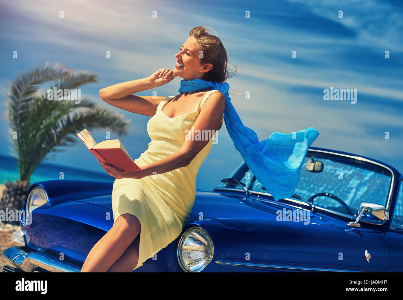 Schöne glückliche Frau mit einem Buch in der Nähe von Retro-Cabrio Auto auf dem Strand. Idyllische Landschaft Stockfoto