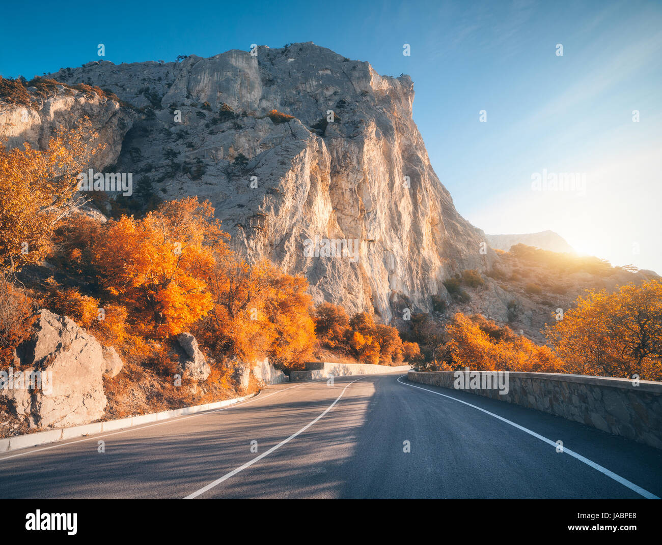 Asphaltierte Straße im Herbst bei Sonnenaufgang. Landschaft mit schönen leeren Bergstraße mit perfekter Asphalt, hohe Felsen, Bäumen und sonnigen Himmel. Vintage tonin Stockfoto