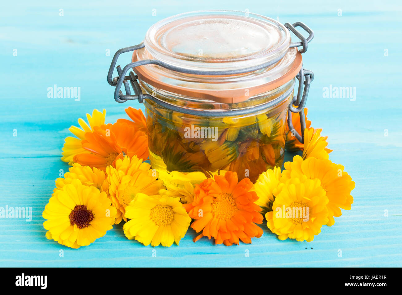 Calendula-Öl in ein Gefäß mit Calendula Blumen auf blauem Hintergrund aus Holz. Stockfoto