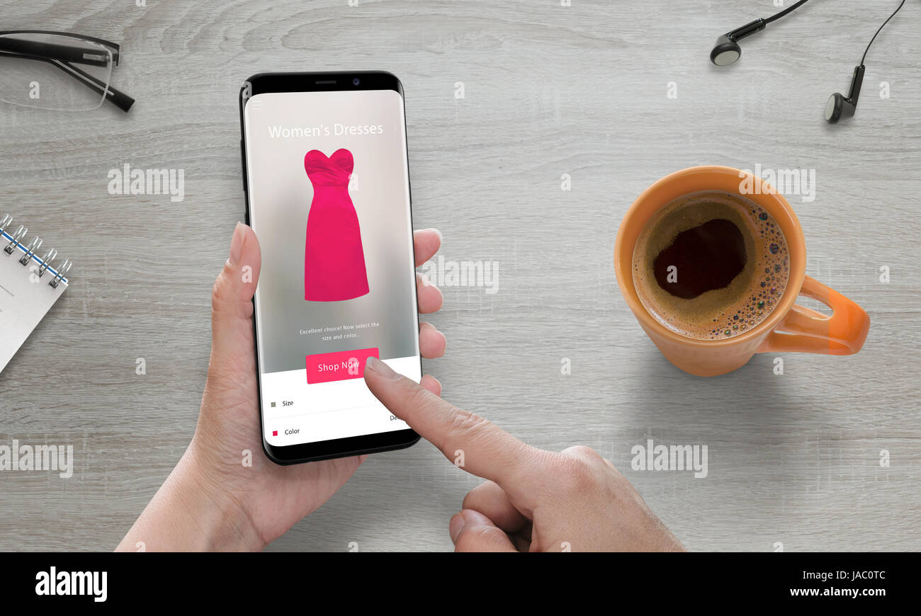 Online-shopping mit modernen Handy. Frau verwenden Online-Shop, um rosa Kleid zu kaufen. Modernes Smartphone mit abgerundeten Ecken. Kaffee neben. Stockfoto
