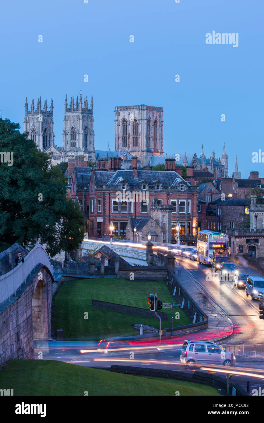 Stadtmauer, Straße über Lendal Bridge & 3 dunklen Abendhimmel, ikonischen Türme des Münsters gegenübergestellt Leuchten von Straßenlaternen & Lichtspuren - York, GB, UK. Stockfoto