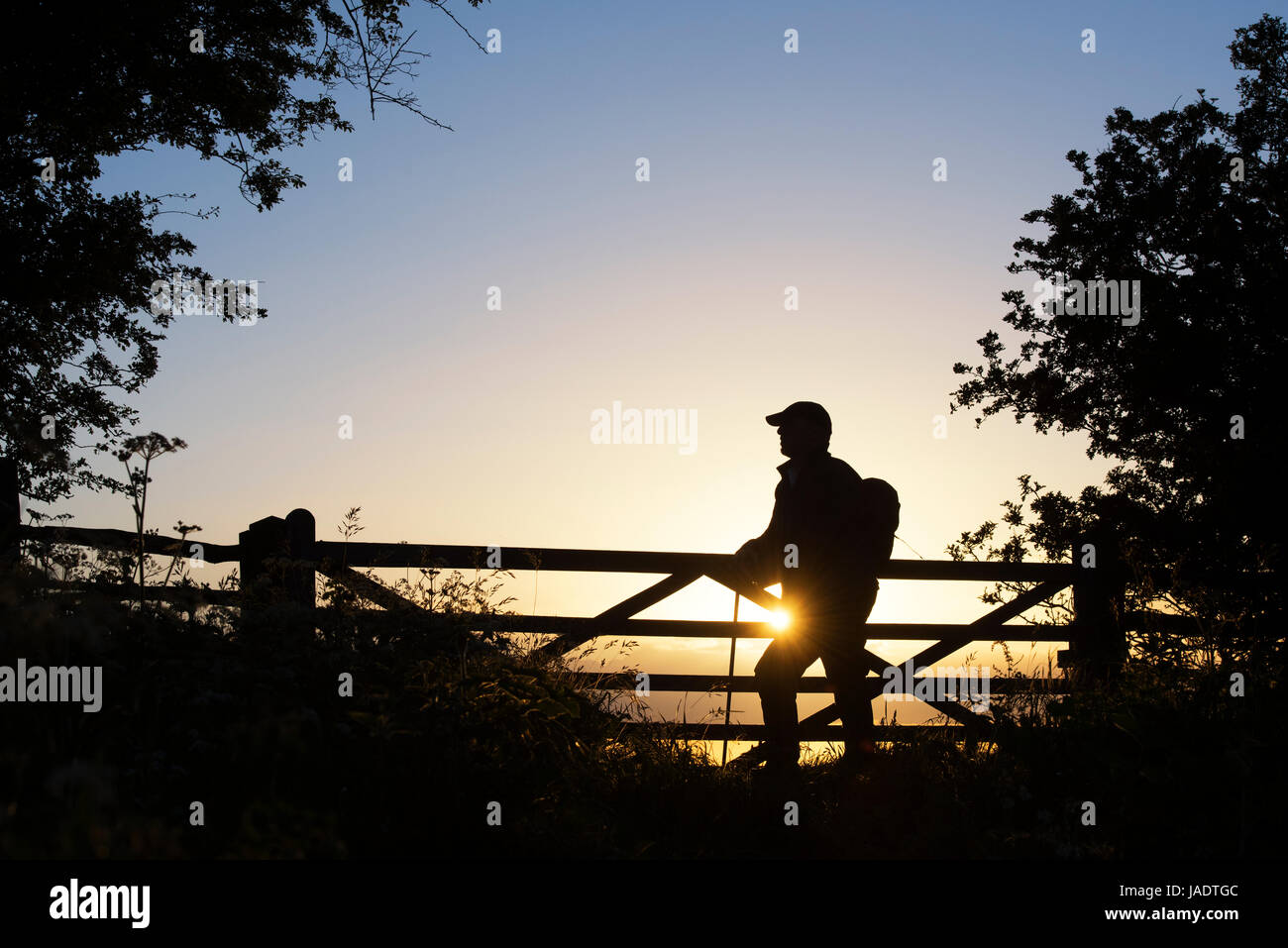 Silhouette Walker durch ein Tor auf dem Cotswold Weg bei Sonnenuntergang auf Broadway Hügel stehen. Cotswolds, Broadway, Gloucestershire, England Stockfoto