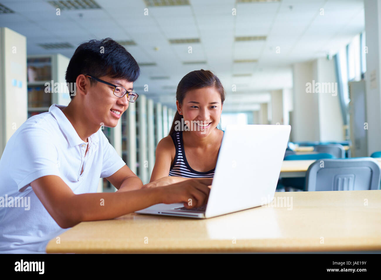 Glückliche junge chinesische oder asiatische Studenten studieren gemeinsam in der Bibliothek mit Computer oder laptop Stockfoto