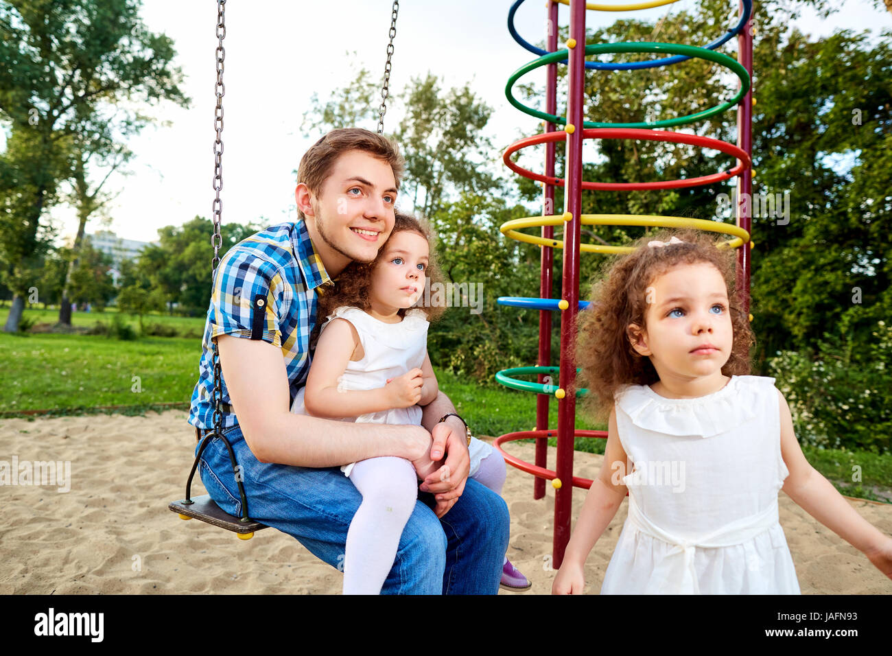 Vater mit Kindern auf einer Schaukel auf dem Spielplatz Stockfoto