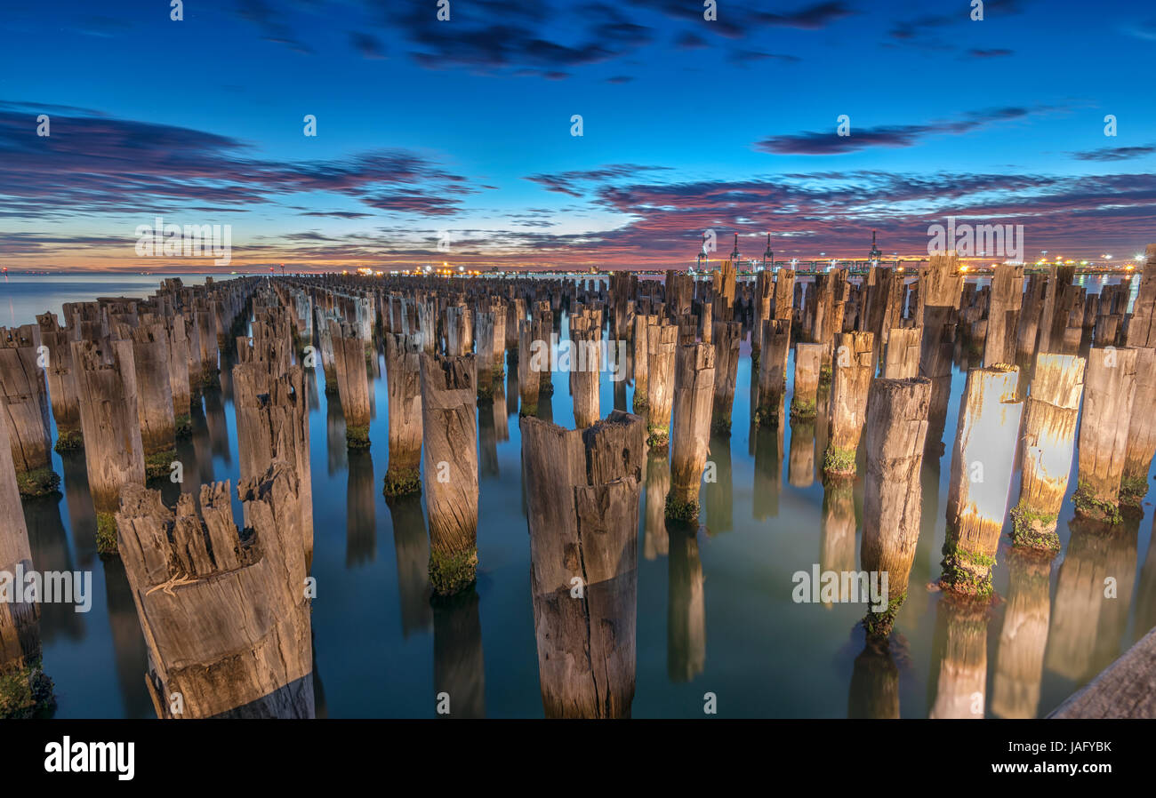 Die schöne Reste eines verlassenen Pier in der Dämmerung mit einem bunten Himmel und ein Kreuzfahrtschiff aus Segeln in der Ferne. Stockfoto