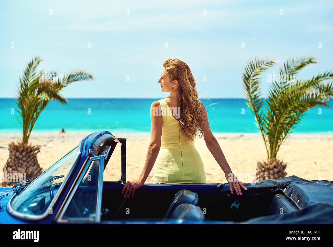 Attraktive Frau in der Nähe von Retro-Auto am tropischen Strand in der Nähe von türkisfarbenen Meer. Idyllische Landschaft Stockfoto